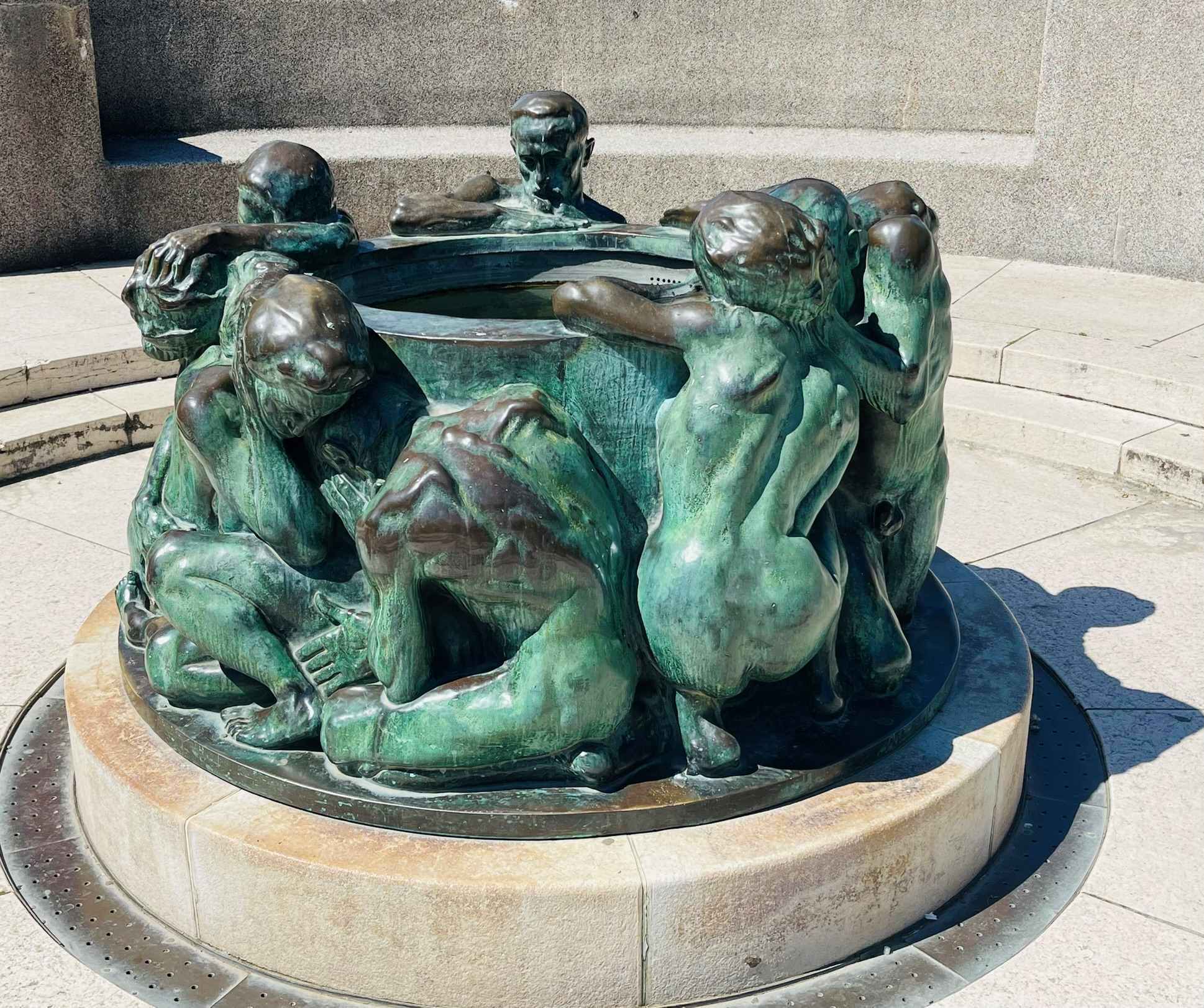 Green oxidized statue of several people surrounding a large vase in Zagreb, Croatia